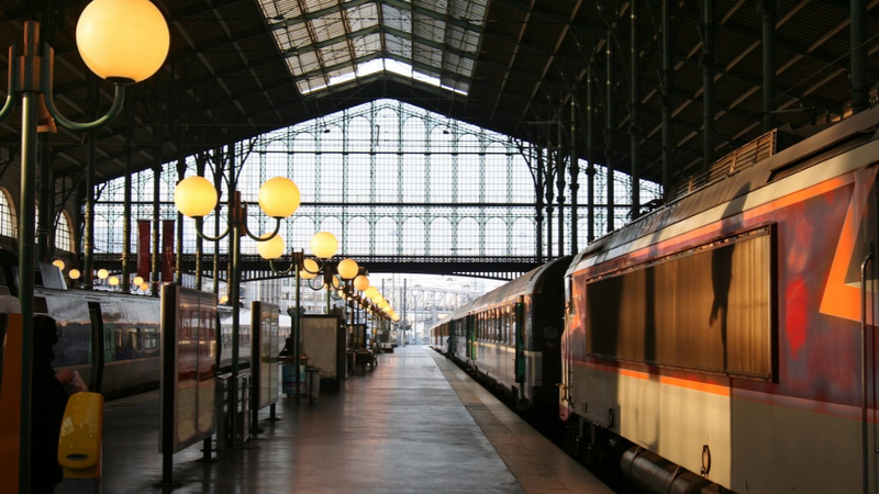 Gare avec des trains à quai sous une verrière, illustrant un service de réservation de train pour professionnels et entreprises.